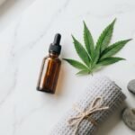 CBD oil dropper bottle with hemp leaves, a towel and river stones on a marble surface