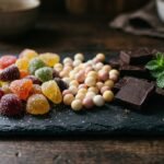 Assorted unbranded gummies, pearl-shaped sweets and dark chocolate squares on a slate board
